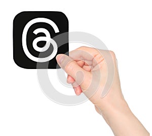 Hand holds paper Threads mobile app icon, on transparent background. Threads is an online social media and social networking