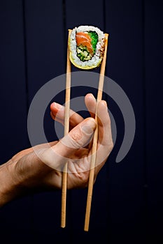 hand holds Philadelphia sushi roll with smoked salmon, avocado, cucumber and green calve with bamboo chopsticks