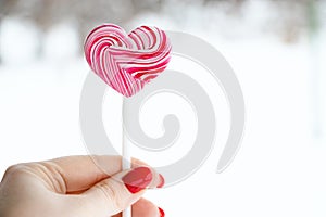 Hand holds pink lollipop. Sweet heart, symbol of valentines day.