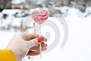 Hand holds pink lollipop. Sweet heart, symbol of valentines day.