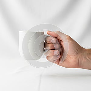 A hand holds a plain white ceramic mug, positioned against a
