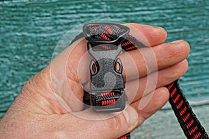 Hand holds a plastic closed carabiner latch on a red black harness