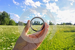 Hand holds a polarizer filter on summer landscape background.