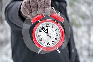 Hand holds a red alarm clock showing 12 o`clock