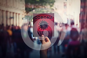 Hand holds red banner warning rapidly spreading Coronavirus on crowded city streets. Deadly Corona virus epidemic outbreak,