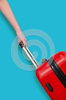 A hand holds a red suitcase on a blue background. Travel concept