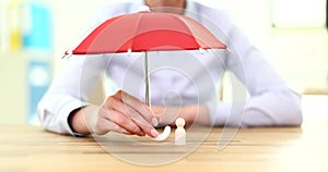 Hand holds red umbrella with figurine. Insurance coverage concept