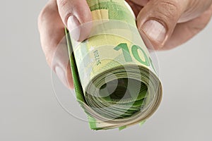 The hand holds a roll of 100 euro banknotes. Euro banknotes rolled up in a white man's hand on a gray background