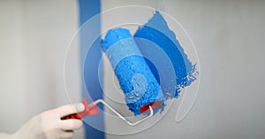 Hand holds roller and wire on wall with blue paint