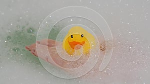 Hand holds a rubber yellow duck out of the water in a bath with foam