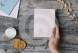 Hand holds a sheet of paper on a wooden table background, milk, cookies, notebooks