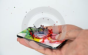 The hand holds a smartphone from the display of which a splash of bright, multi-colored colors breaks out and drops fly in all