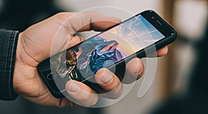 A hand holds a smartphone displaying a vibrant landscape on the screen