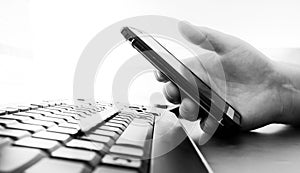 Hand holds a smartphone over a black computer keyboard