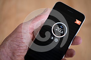 Hand holds smartphone with thermostat app to control central heating temperature in house