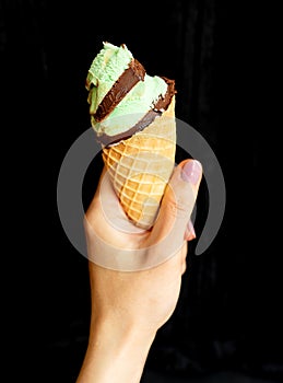 The hand holds soft ice cream in a chocolate-mint waffle cup. On a black background, close-up.