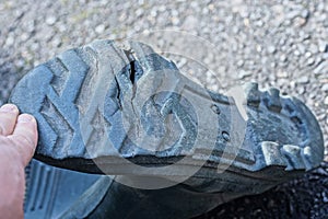 Hand holds the sole with a crack and a hole on an old green rubber boot