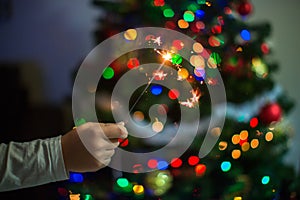 A hand holds a sparkler against the background of the Christmas tree