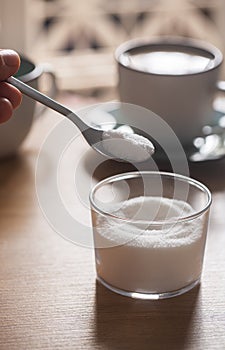 Hand holds spoon with sweetener on coffee background
