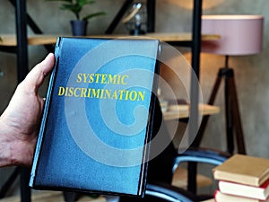 Hand holds Systemic Discrimination book in the office.