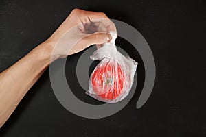 Hand holds tomato in individual plastic package, quarantine isolation safety delivery and environment pollution problem