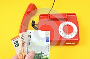 A hand holds up a hand of euro banknotes on the background of a red vintage, old Soviet landline phone. Payment for telephone call