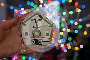 Hand holds up a homemade sugar cookie, decorated as a white barn ranch house decorated for Christmas