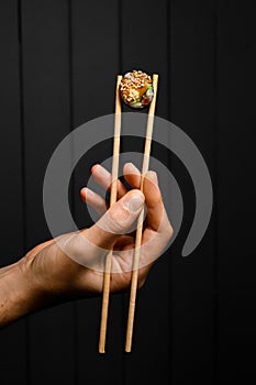 hand holds vegetarian sushi roll with bamboo chopsticks on dark background
