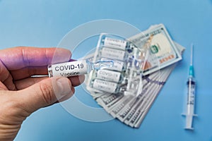 Hand holds vial of vaccine coronavirus on background of money and syringe. Price of drugs from covid-19, concept