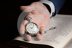 A hand holds a vintage pocket watch on the background of an old book