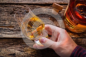 Hand holds whiskey in a glass for tasting on a wooden background