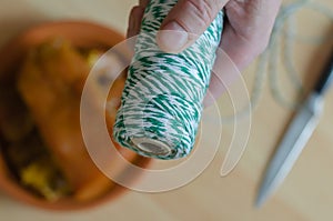 A hand holds a white and green skein of twine over the kitchen table.