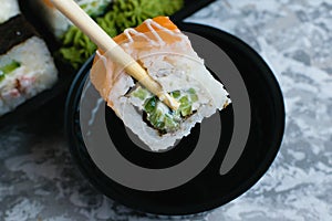 Hand holds wooden sticks sushi california roll with fish, cheese and mayonnaise. Large set of rolls with soy sauce and