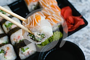 Hand holds wooden sticks sushi california roll with fish, cheese and mayonnaise. Large set of rolls with soy sauce and