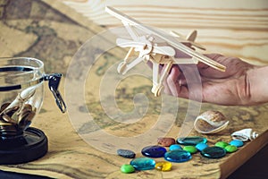 Hand holds wooden toy plane on a world map with colored stones and shells from the sea in a retro style