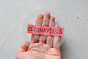 A hand holds the word Coronavirus, which is written on a red sheet of paper, on a light gray modern background. Epidemic, danger,