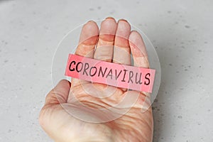 A hand holds the word Coronavirus, which is written on a red sheet of paper, on a light gray modern background. Epidemic, danger,