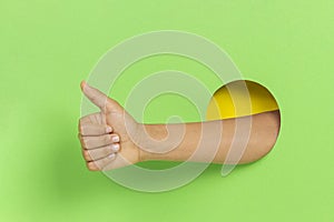 Hand through hole in green background keeps thumb up, demonstrates approval sign showing like gesture