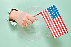 A hand from a hole in green paper holds an American flag with blue stars. America Independence Day Concept