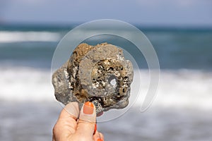 Hand with holey stone on the beach on Crete island at summer, Greece