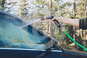 Hand with hose are spraying and cleaning a car