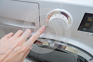 A hand of a housewife switching on a washing machine, pushing the power button after choosing cycle program