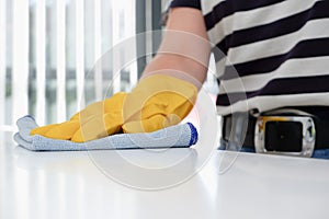 The hand of a housewife in a yellow protective rubber glove holds a rag with microfiber fiber