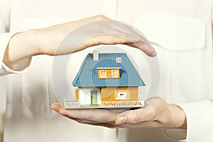 Hand hovering small family house, home insurance concept