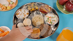 Hand of an Indian woman placing a bowl of Chaulai Laddu in Navratri food platter