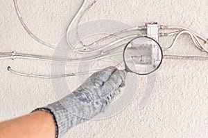 The hand of an industrial worker in a construction glove examines a large antenna splitter with a magnifying glass