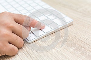 Hand with injury on finger using white computer keyboard on wood