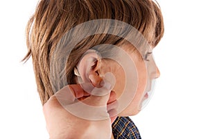 Hand inserting a hearing aid in a young boy`s ear