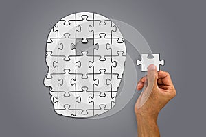 Hand inserting missing brain jigsaw in white man`s head shape