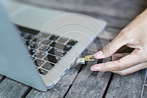 Hand inserting USB flash drive into computer laptop on the desk.